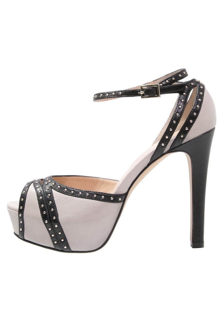 Sandał na wysokim obcasie z jasnoszarej skóry z czarnymi akcentami i paskami z ćwiekami. Posiada regulowany pasek wokół kostki oraz platformę.