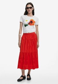 Hvid bomulds T-shirt med blomster grafik, parret med en rød lagdelt nederdel med broderede blomster mønstre og sorte slip-on sko.