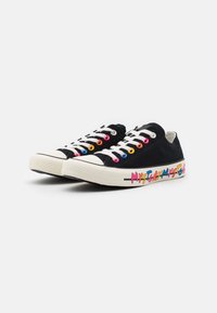 Zapatillas de lona negras con ojales multicolores, cordones blancos y una suela de goma texturizada. Presentan un texto colorido "MI HISTORIA" en el costado.