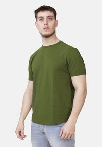 T-shirt in cotone verde oliva con colletto rotondo e maniche corte, caratterizzata da un design minimalista. Texture liscia con una forma aderente.
