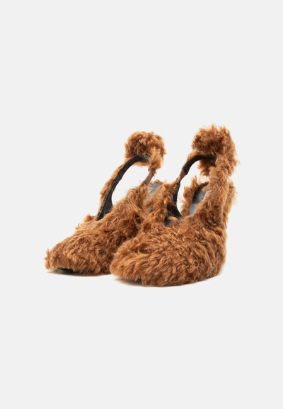 Ζεύγος καφέ χνουδωτών παπουτσιών με ψηλό τακούνι, ανοιχτή πλάτη και λουράκια στον αστράγαλο σε λευκό φόντο.