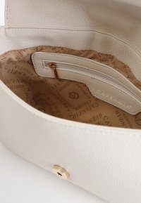 Hvid tekstureret lædertaske med en beige mønstret indvendig, der har en lynlåslomme og et guldfarvet hardware-detalje.