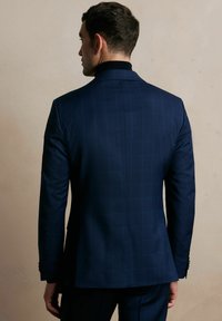 Granatowa marynarka w kratę o strukturalnym designie, teksturowanej tkaninie i łatą na klapie, z guzikowymi akcentami na rękawach i rozcięciu z tyłu.