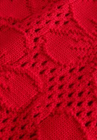 Rødt strikket stof med et diamantmønster med hulmønstrede sektioner. Teksturen er blød og ensartet og fremhæver stingdetaljerne.