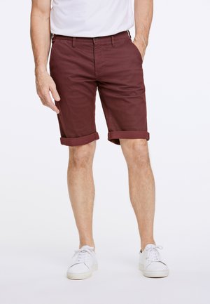 Burgundy puuvillashortsit, joissa on käärityt hihansuut, etutaskut ja nappikiinnitys, yhdistetty valkoisiin tennareihin. Sujuva pinta, rento malli.