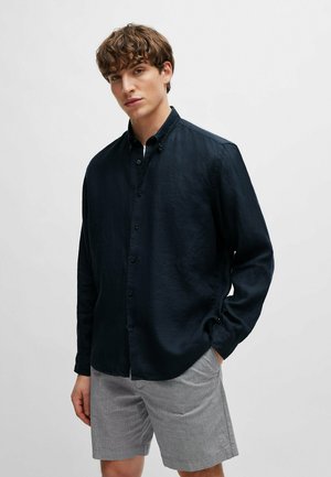 Chemise bleu marine à manches longues, à boutons, en tissu doux et texturé, associée à un short gris à motifs. La chemise possède un col classique et des poignets.