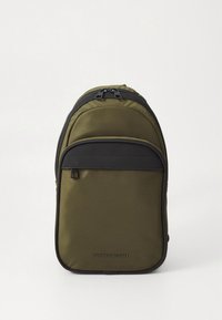 Olive green backpack with a black front pocket, zippers at the top, and a logo on the lower front. Smooth fabric with a rectangular shape.