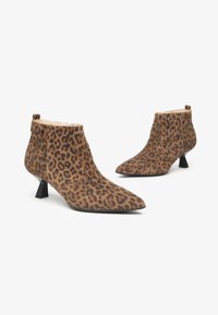 Stivali alla caviglia con stampa leopardata in suede, caratterizzati da una punta affusolata, tacco corto a blocco e una texture liscia. Chiusura con zip sul retro.