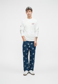 Bela dolga majica s grafičnim tiskom, v kombinaciji z modrimi kavbojkami, ki imajo ponavljajoče se vzorce yin-yang. Nosi se z belimi športnimi čevlji.