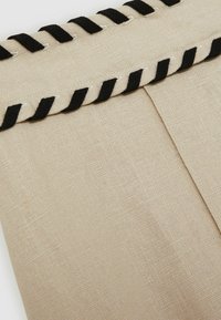 Beige linnen stof met een gestructureerd oppervlak, voorzien van een zwarte gevlochten bies langs de bovenrand. Eenvoudig ontwerp, met twee verticale naden.