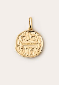 Pendentif en or avec une texture martelée et une forme arrondie. Il présente un nom de marque gravé, "SINGULARU," et une simple boucle de suspension.