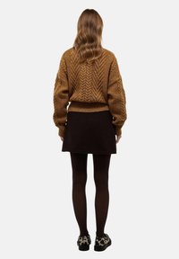 Pull en tricot marron avec un motif en chevron texturé, associé à une jupe noire et des collants foncés. Les chaussures présentent un design imprimé léopard.