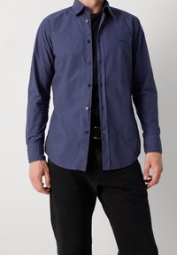 Marinblå långärmad skjorta i lätt tyg, med krage som knäpps och subtilt varumärke på vänster bröst.