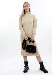 Abito maglione in cable-knit crema con colletto alto, abbinato a una borsa a tracolla con stampa leopardata marrone e stivaletti neri con dettaglio a cinturino.
