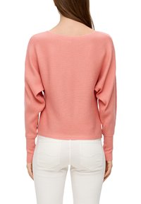 Rosa gerippter Pullover mit weitem Ausschnitt und langen Ärmeln, kombiniert mit weißen Jeans. Der Stoff wirkt weich und strukturiert.