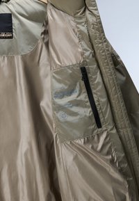 Beige Jackeninnenseite mit einer Reißverschlusstasche, einem Markenetikett und einem glatten Stofffutter.