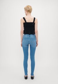 Svart avkortet topp med brede stropper og en volangkant, kombinert med lyseblå skinny jeans. Svart slip-on sko fullfører antrekket.