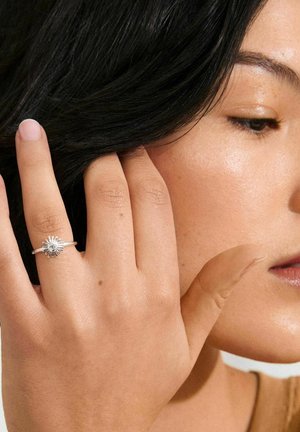 Silver ring with a sunray design, featuring a central gemstone. Hand with natural nails rests against hair, showcasing the ring's details.