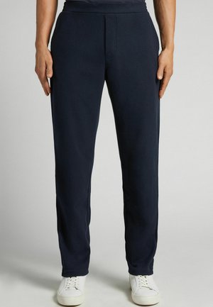 Pantalones de chándal azul marino de tejido suave, con corte recto, cintura elástica y un diseño minimalista, combinados con zapatillas blancas.