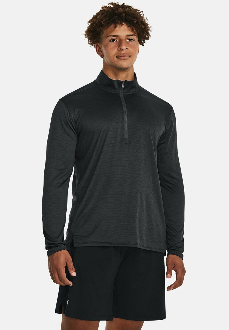 Schwarzes langärmliges Sportoberteil mit einem halben Reißverschlusskragen, aus leichtem, strukturiertem Material. Kombiniert mit schwarzen Shorts.