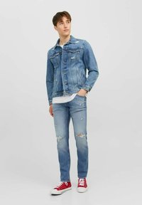 Chaqueta de mezclilla azul claro con detalles desgastados, combinada con jeans rasgados azul claro y zapatillas de lona rojas. Camiseta blanca simple debajo.