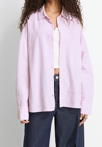 Camicia a righe rosa chiaro con colletto, taschino sul petto, e maniche oversize, abbinata a pantaloni in denim scuri.