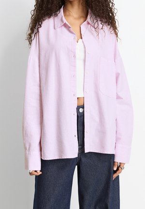 Chemise à rayures roses claires avec col, poche poitrine unique et manches surdimensionnées, assortie à un pantalon en denim foncé.