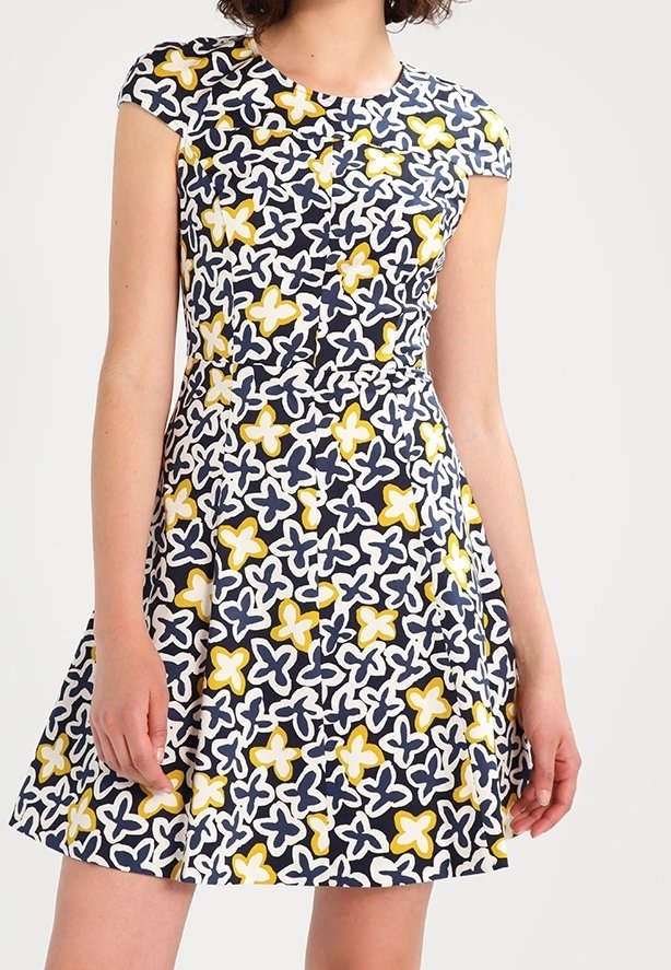 Robe à manches courtes avec un fond bleu marine et un motif floral en blanc, jaune et bleu clair. Jupe évasée avec corsage ajusté.