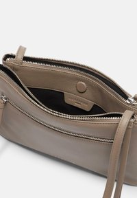 Skórzana torebka na ramię w kolorze taupe z dwiema zamykanymi na zamek kieszeniami i czarną podszewką. Posiada odpinany pasek i polerowane elementy ozdobne.
