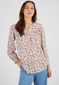 Blusa floreale color crema con motivi rossi e blu, dotata di una pattina con bottoni, maniche lunghe e una vestibilità comoda. Tessuto dal tocco morbido.