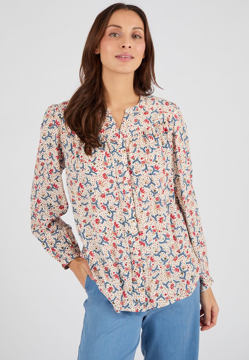Blusa floreale color crema con motivi rossi e blu, dotata di una pattina con bottoni, maniche lunghe e una vestibilità comoda. Tessuto dal tocco morbido.