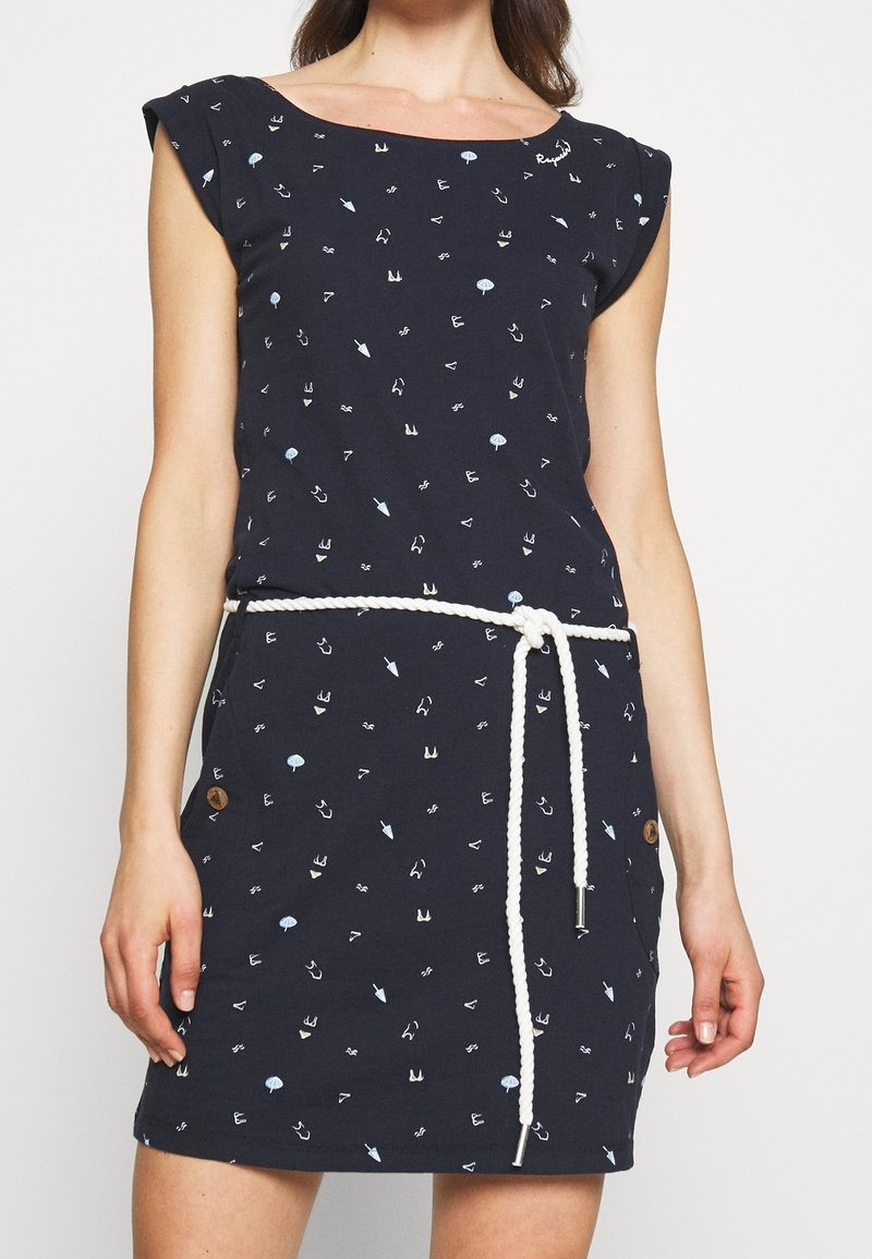 Granatowa sukienka z krótkimi rękawami, występująca w wzór składający się z jasnoniebieskich i białych kształtów. Zawiera białą sznurówkę w talii oraz drewniane akcenty w postaci guzików.