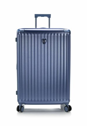 Valise rigide bleue avec quatre roues et une poignée déployée, debout sur fond blanc.