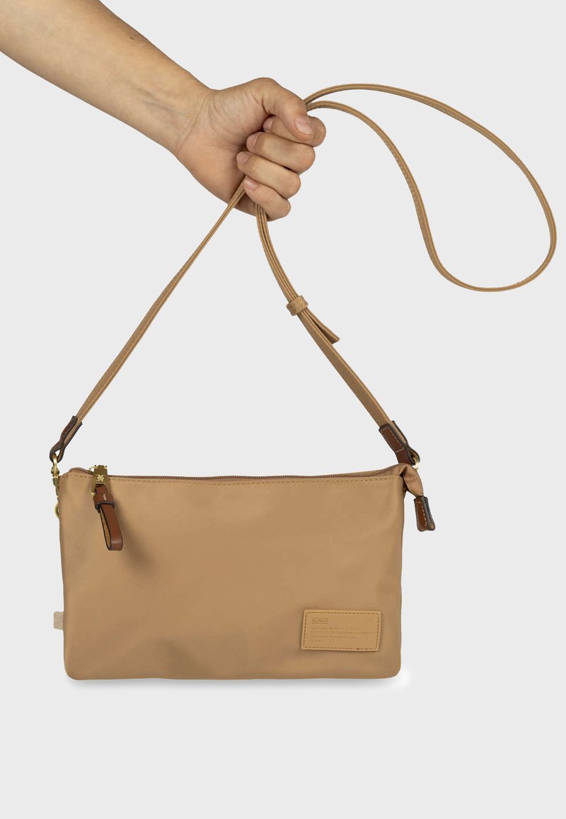 Sac à main en matériau synthétique marron clair avec fermeture zippée, bandoulière réglable et accents en cuir marron. Texture lisse avec une forme rectangulaire.