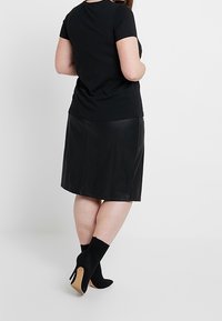 Camiseta negra de manga corta combinada con una falda de imitación de cuero negra a la altura de la rodilla y botas negras hasta el tobillo con tacón beige.