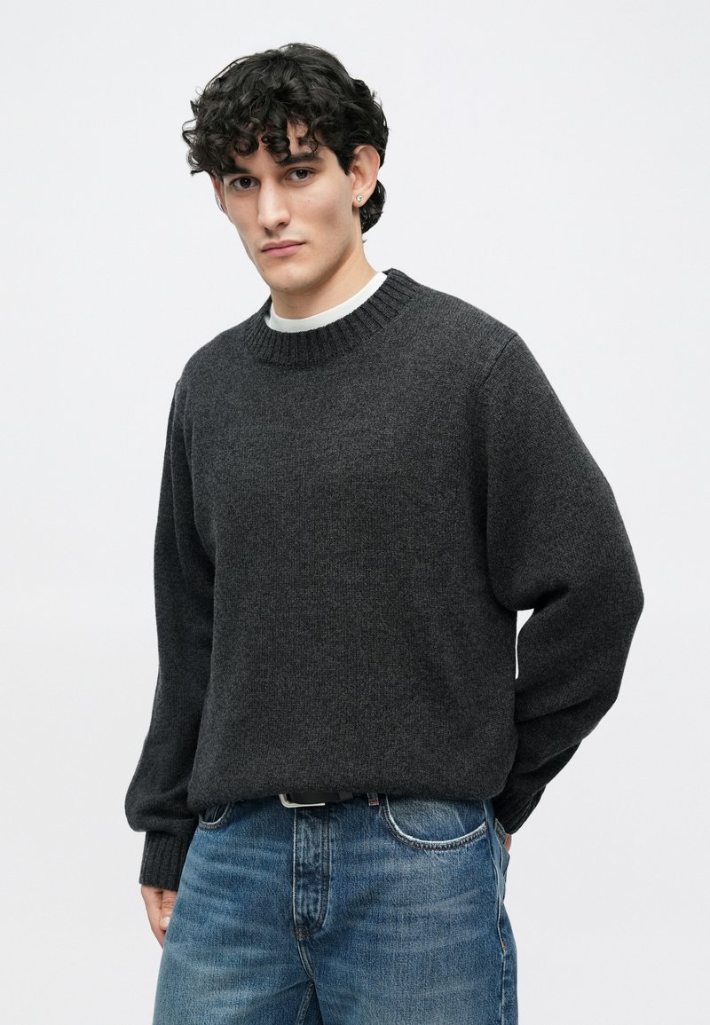 Pull en maille gris foncé avec un col arrondi et des poignets côtelés, associé à un jean en denim bleu clair. Coupe classique et décontractée avec une texture douce.