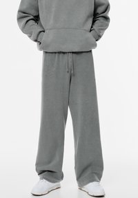 Harmaa oversized huppari ja siihen sopivat leveälahkeiset housut pehmeästä materiaalista, joissa on kiristysnauha vyötäröllä ja ribbauskankaiset hihansuut, yhdistettynä valkoisiin lenkkareihin.
