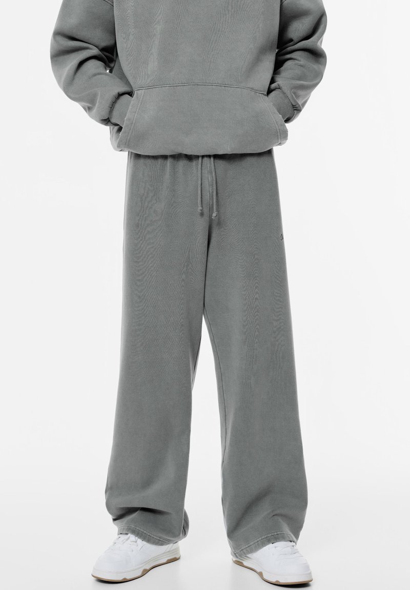 Harmaa oversized huppari ja siihen sopivat leveälahkeiset housut pehmeästä materiaalista, joissa on kiristysnauha vyötäröllä ja ribbauskankaiset hihansuut, yhdistettynä valkoisiin lenkkareihin.