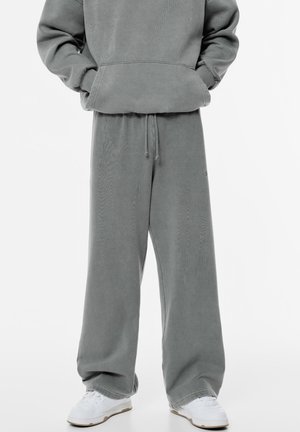 Grijze oversized hoodie en bijpassende wijde broek van zachte stof, met een drawstring taille en ribgebreide manchetten, gecombineerd met witte sneakers.