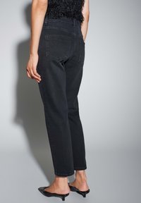 Jean noir taille haute avec une coupe droite, doté de deux poches arrière et d'une texture légèrement délavée, associé à des chaussures noires pointues.