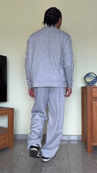 Sweatshirt cinza e calças de fato combinando com um corte relaxado, feitas de um tecido suave, apresentando riscas laterais e um design simples.