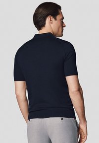 Granatowa koszulka polo z krótkim rękawem, z prążkowanym kołnierzykiem i mankietami, pleciona faktura, widok z tyłu ukazujący dopasowany krój i bezszwowe ramiona.