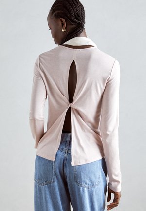 Lys rosa langermet topp med en utskjæring bak og knute-detail. Glatt stoff, rund krage, kombinert med høytlivede blå jeans.
