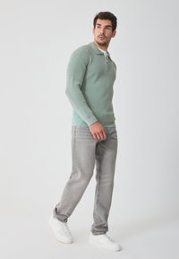 Light green ribbed long-sleeve pullover with a zip collar, paired with light gray straight-leg jeans and white athletic sneakers.
