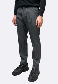 Pantaloni grigi a vita alta con pieghe frontali, cintura con coulisse e design a gamba dritta, abbinati a scarpe nere stringate.