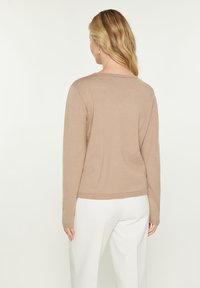 Beige trui met lange mouwen en een ronde hals, gemaakt van zachte stof. Heeft een getailleerd ontwerp met ribbelafwerking aan de onderkant en mouwen.