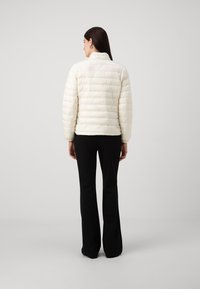 Vit puffjacka med horisontell kviltad mönster, hög krage och långa ärmar, kombinerad med svarta utsvängda byxor.