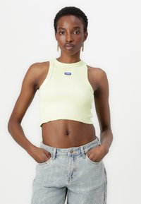 Limegrön ribbad crop top med halterneck-design och logopatch. Matchad med högmidjade blekta blå denimjeans.