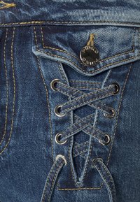 Džíny z denimu mají modrou barvu, šněrování vpředu, stříbrné očko a kovový knoflík s vyrytým logem značky. Žluté švy dodávají akcent.