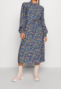 Floral-printed dress with a cinched waist, long puff sleeves, and a high collar, made of lightweight fabric in blue, yellow, and pink tones.